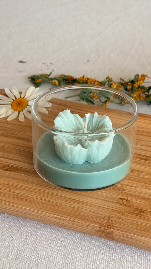 Handmade soy candle in glass jar with flower-shaped wick, mint green wax, on wooden board with daisy
