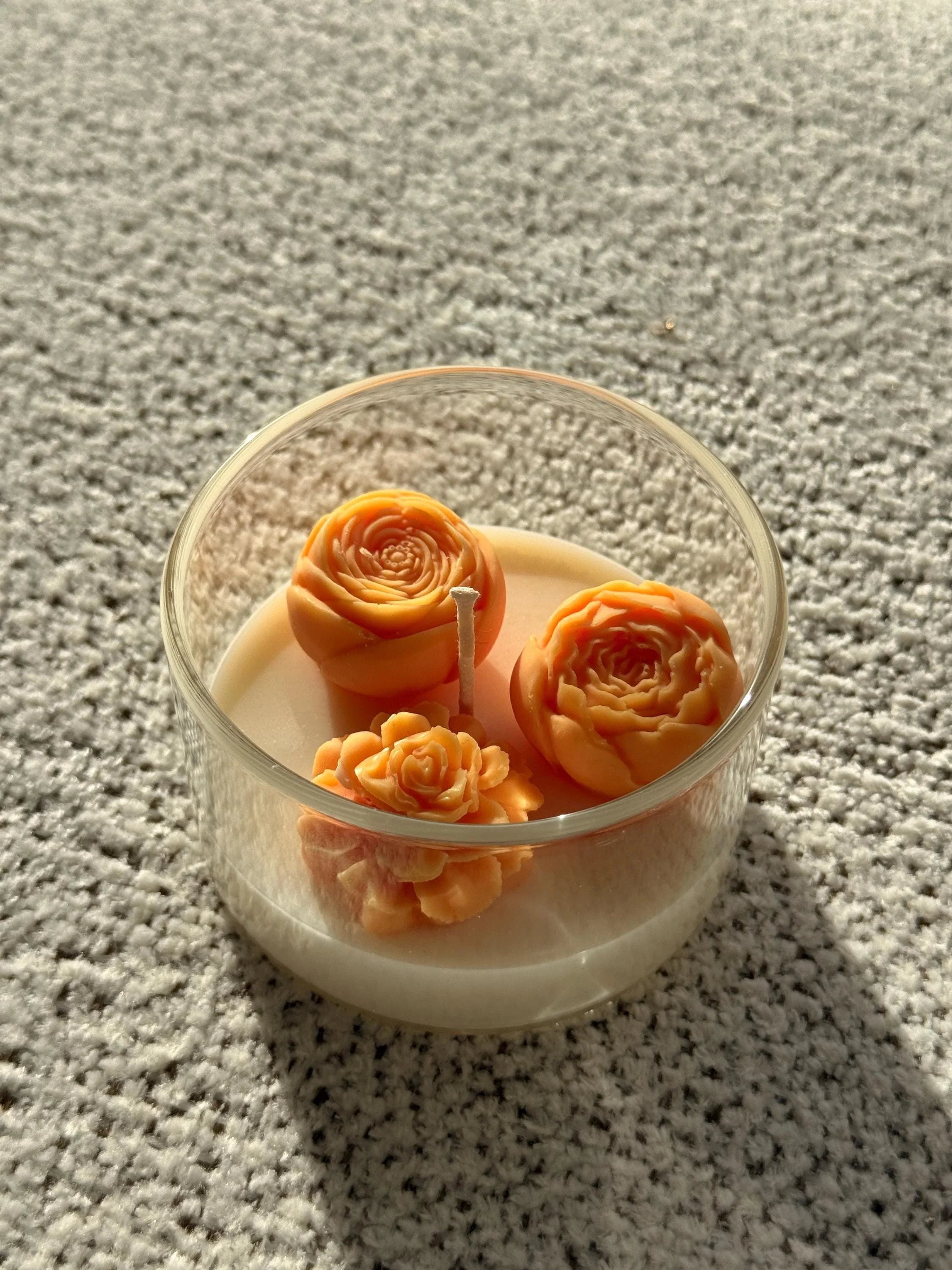 Handmade soy candle with orange rose blooms in clear glass jar, cozy home décor