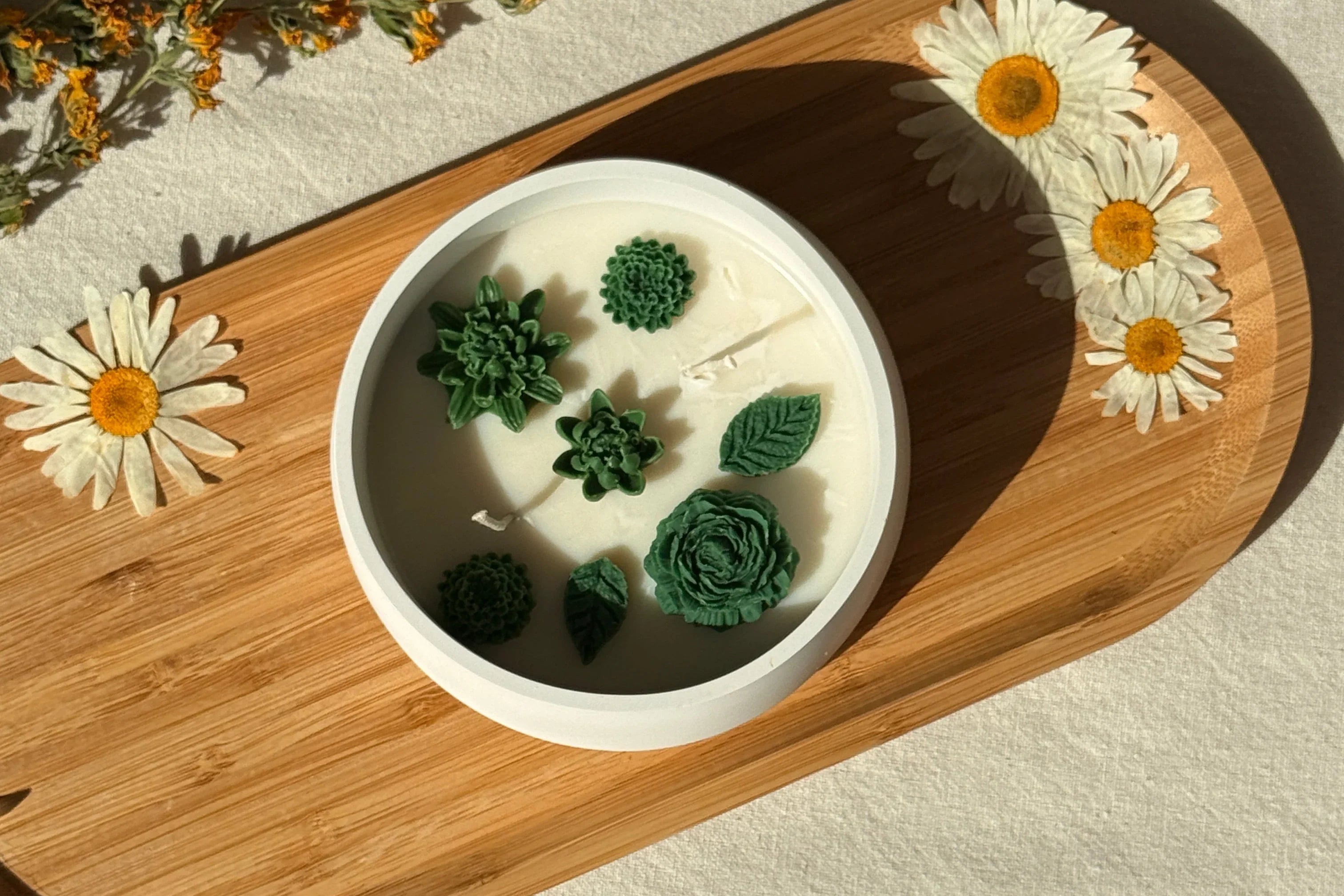 Handmade soy candle with green succulent designs, styled on wood tray with daisies for cozy Scandinavian home décor