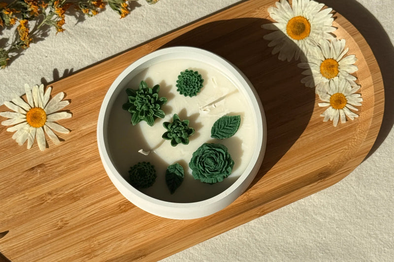 Handmade soy candle with green succulent designs, styled on wood tray with daisies for cozy Scandinavian home décor