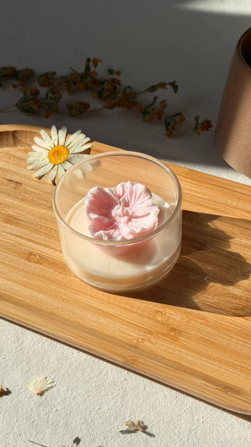 Handmade soy candle with pink flower design in glass jar, styled on wooden tray with dried flowers for cozy home décor.