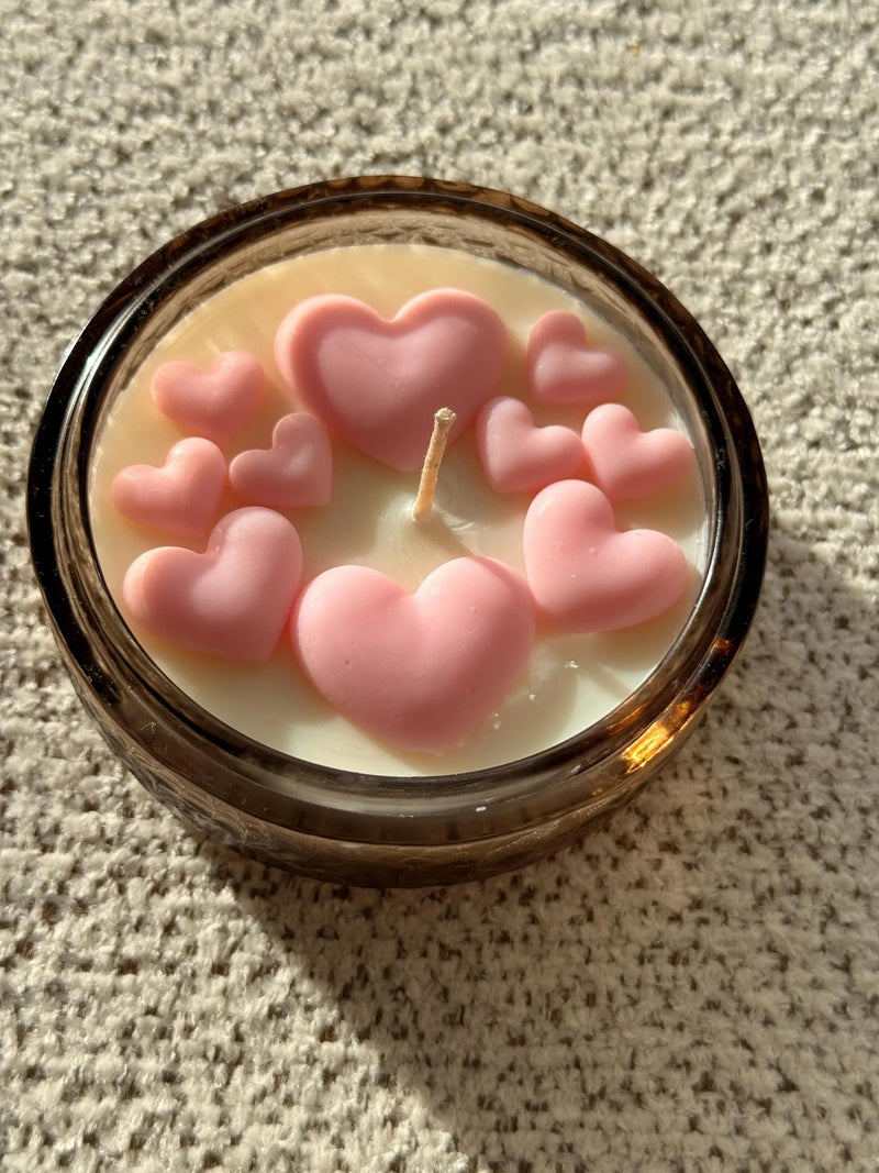 Handmade soy candle with pink heart decorations in amber glass jar, cozy Scandinavian home décor