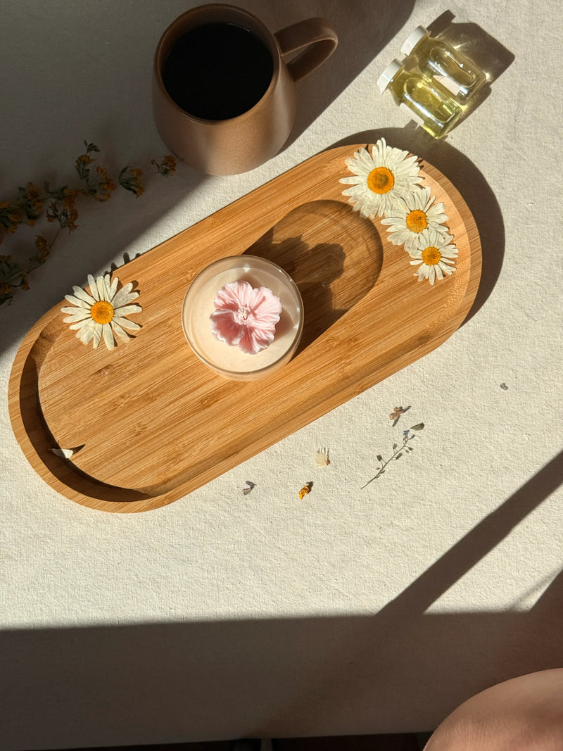 Handmade soy candle with pink flower on wooden tray, daisies, coffee mug, and essential oils for cozy Scandinavian home decor