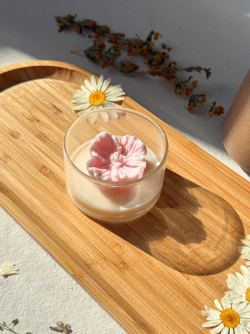 Pink flower-shaped soy candle in glass jar on wooden tray with dried daisies, Scandinavian home decor