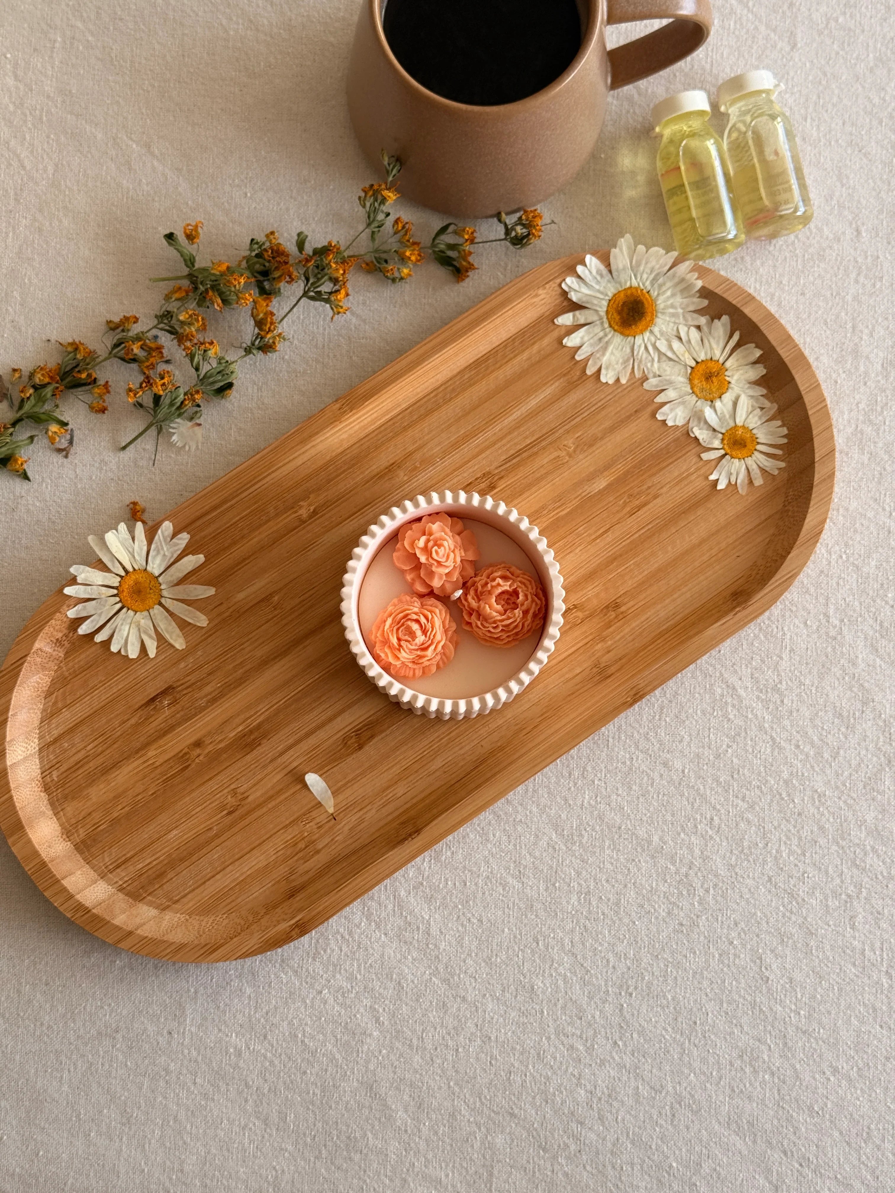 Handmade soy candle with floral design on wooden tray, styled with dried daisies and coffee mug for cozy home décor