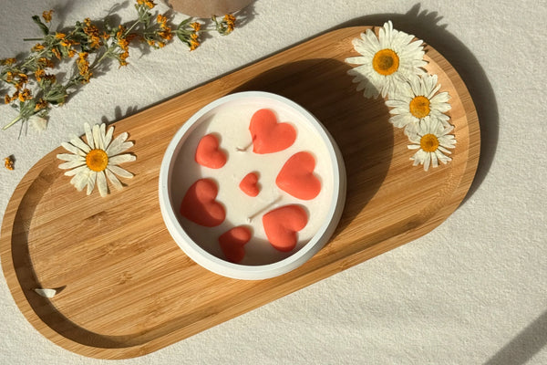 Handmade soy candle with coral hearts, styled on wood tray with daisies for cozy Scandinavian home decor
