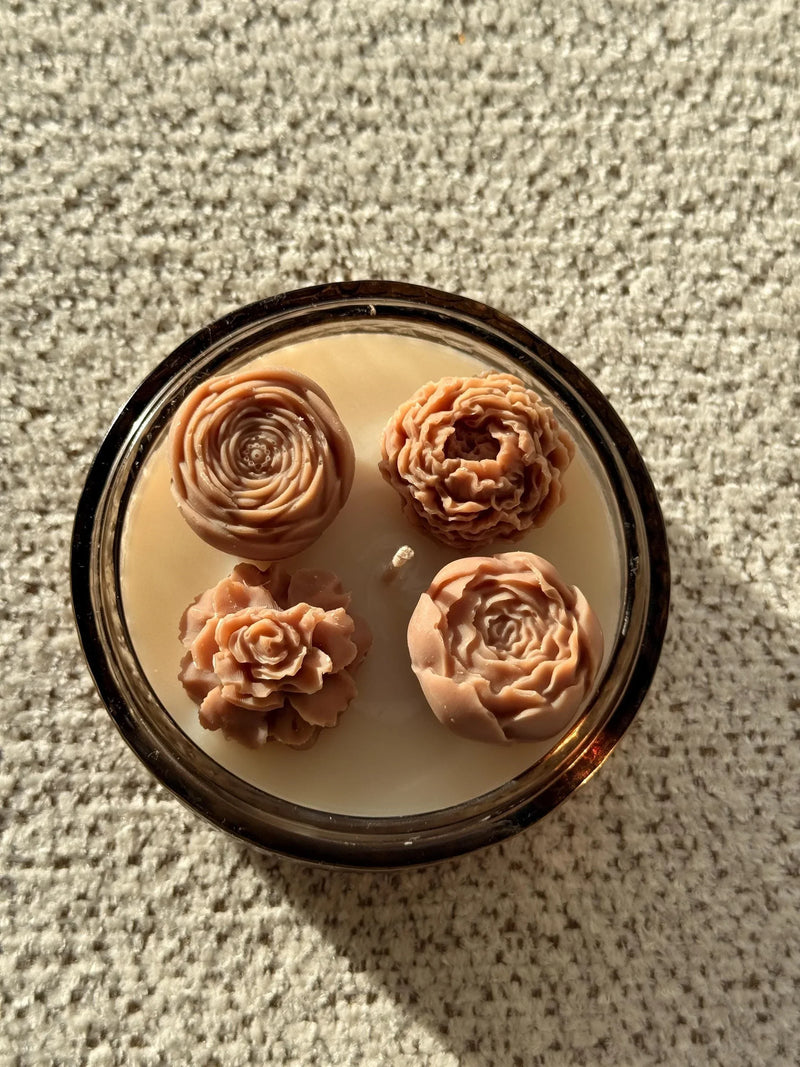Handmade soy candle with four sculpted rose wax flowers in amber glass jar, cozy Scandinavian home decor