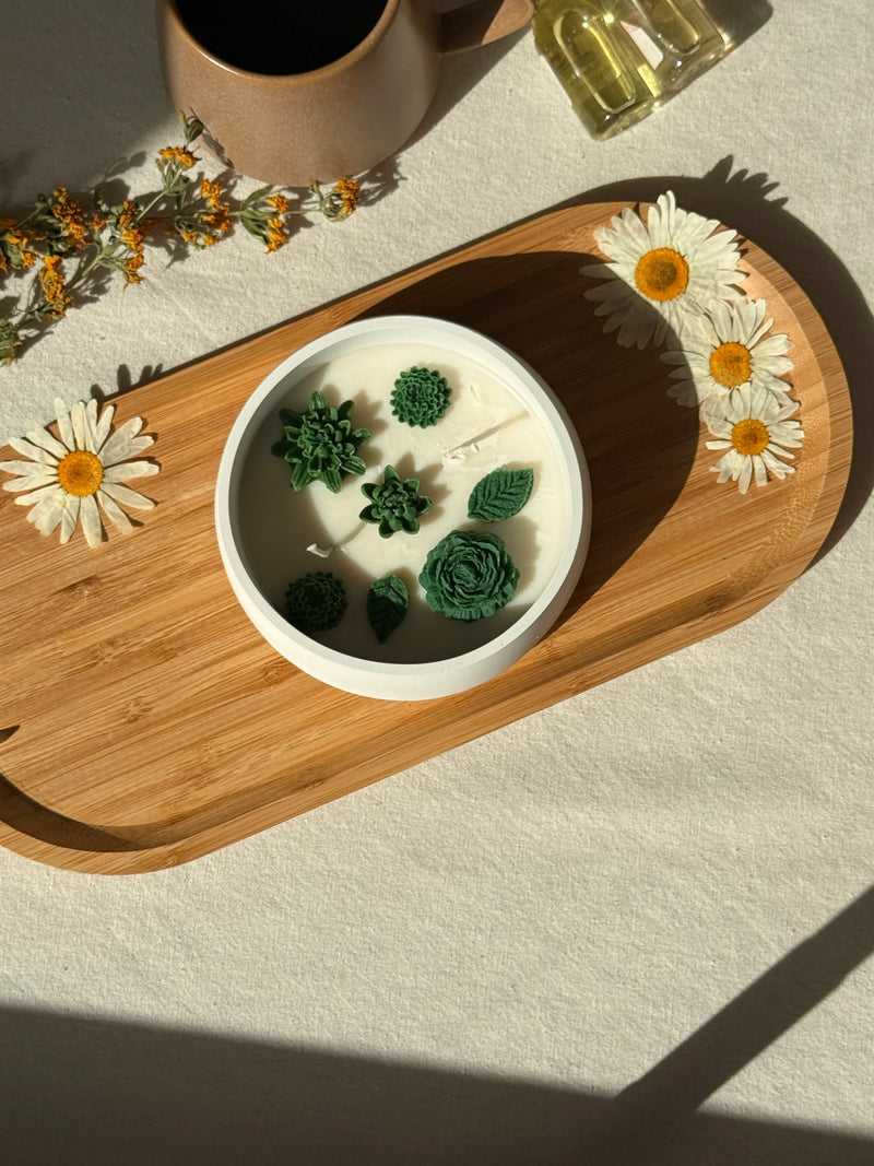 Handmade soy candle with green succulent designs on wooden tray, styled with dried daisies and cozy home decor