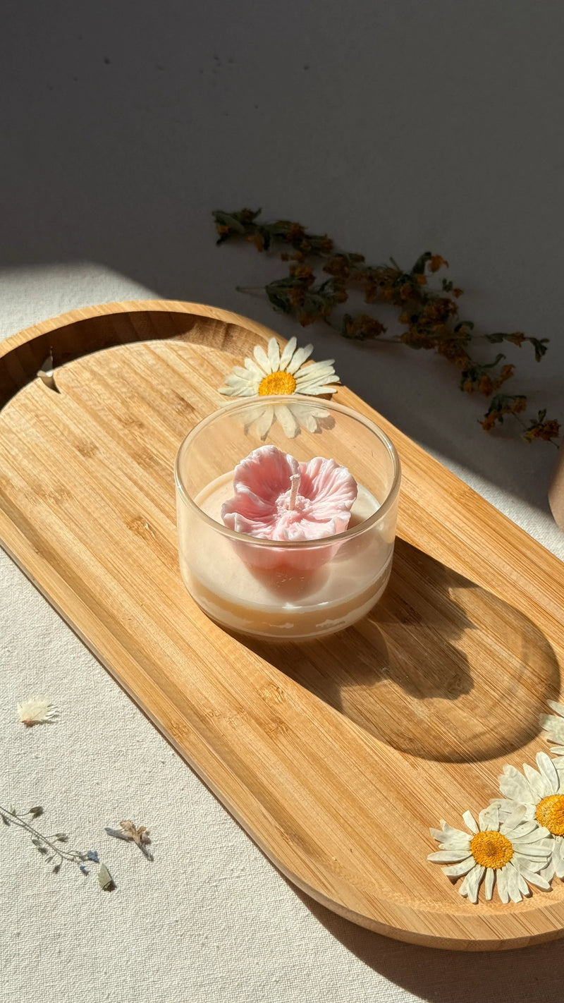 Handmade soy candle with pink flower design in glass jar, styled on wooden tray with dried daisies for cozy home decor