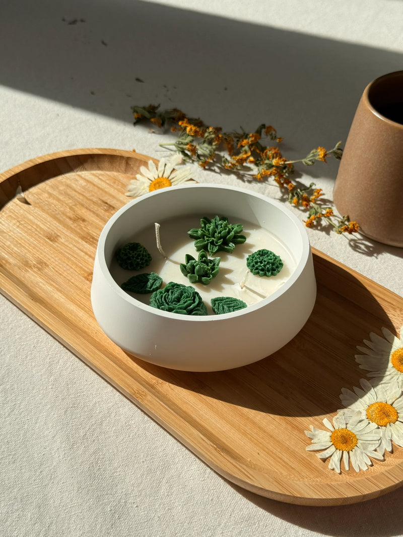 Handmade soy candle with green succulent wax accents, styled on wooden tray with dried daisies for cozy Scandinavian home decor