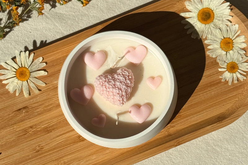Handmade soy candle with pink heart decorations, styled on wood tray with daisies for cozy home décor