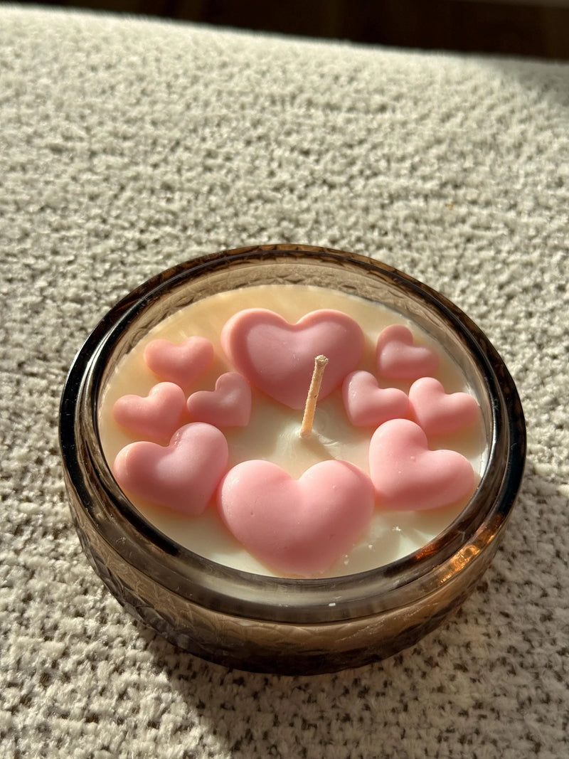 Handmade soy candle with pink heart decorations in amber glass jar, cozy home décor