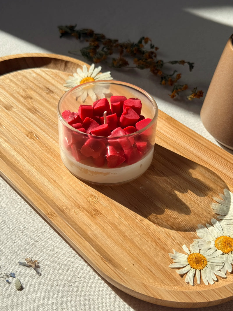 Red heart-shaped soy wax melts in glass jar on wooden tray with dried daisies, cozy home décor