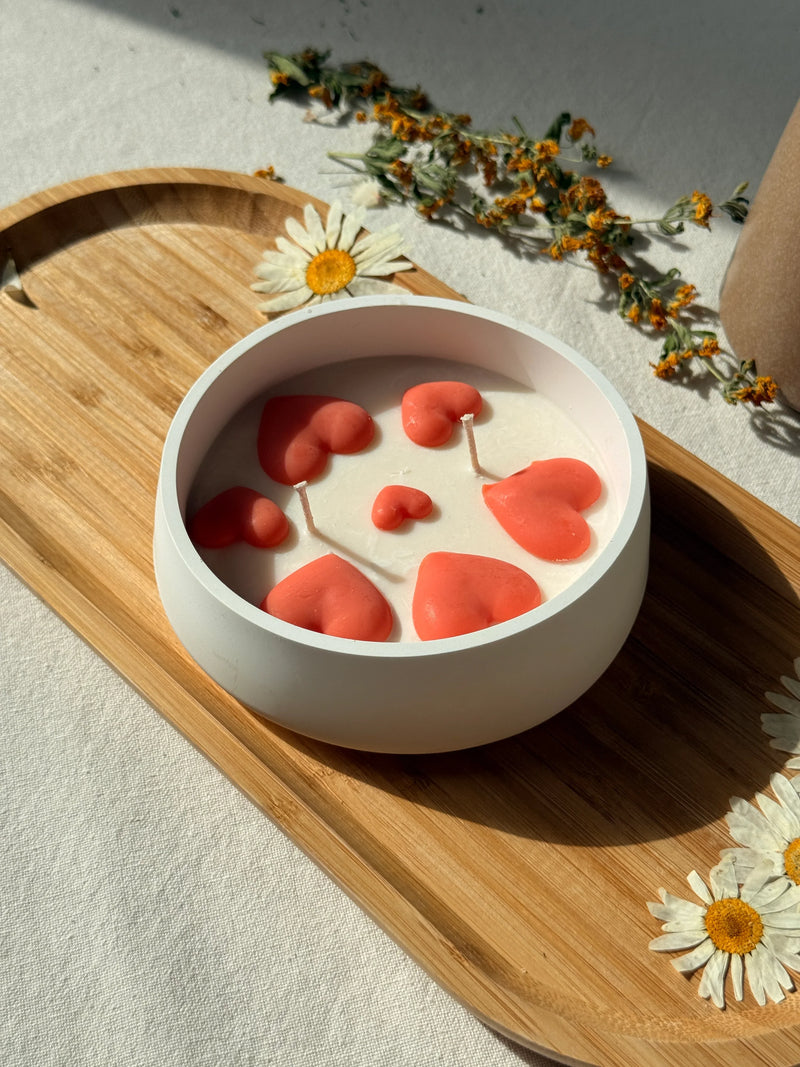 Handmade soy candle with coral hearts in white ceramic bowl, styled with dried flowers on wooden tray