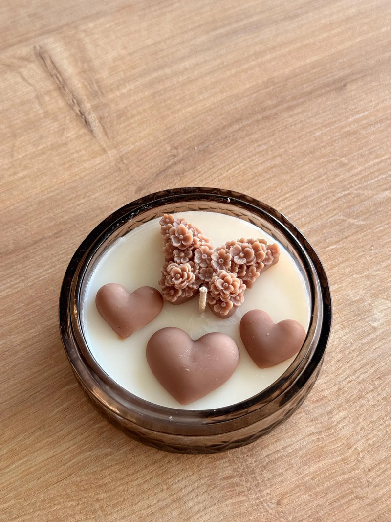 Handmade soy candle with heart and floral wax decorations in amber glass jar