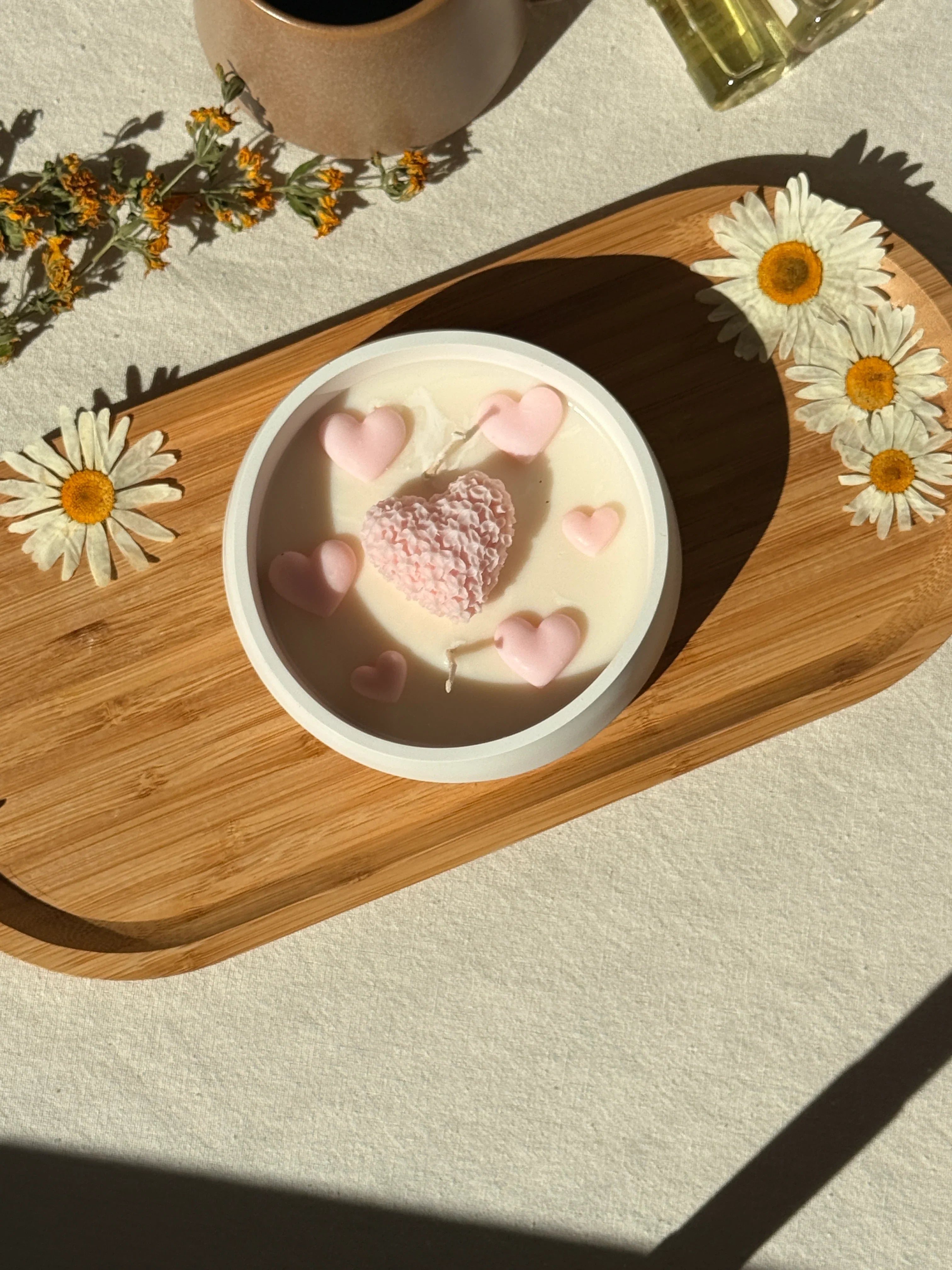 Handmade soy candle with pink heart decorations, styled with dried daisies on a wooden tray for cozy home décor.