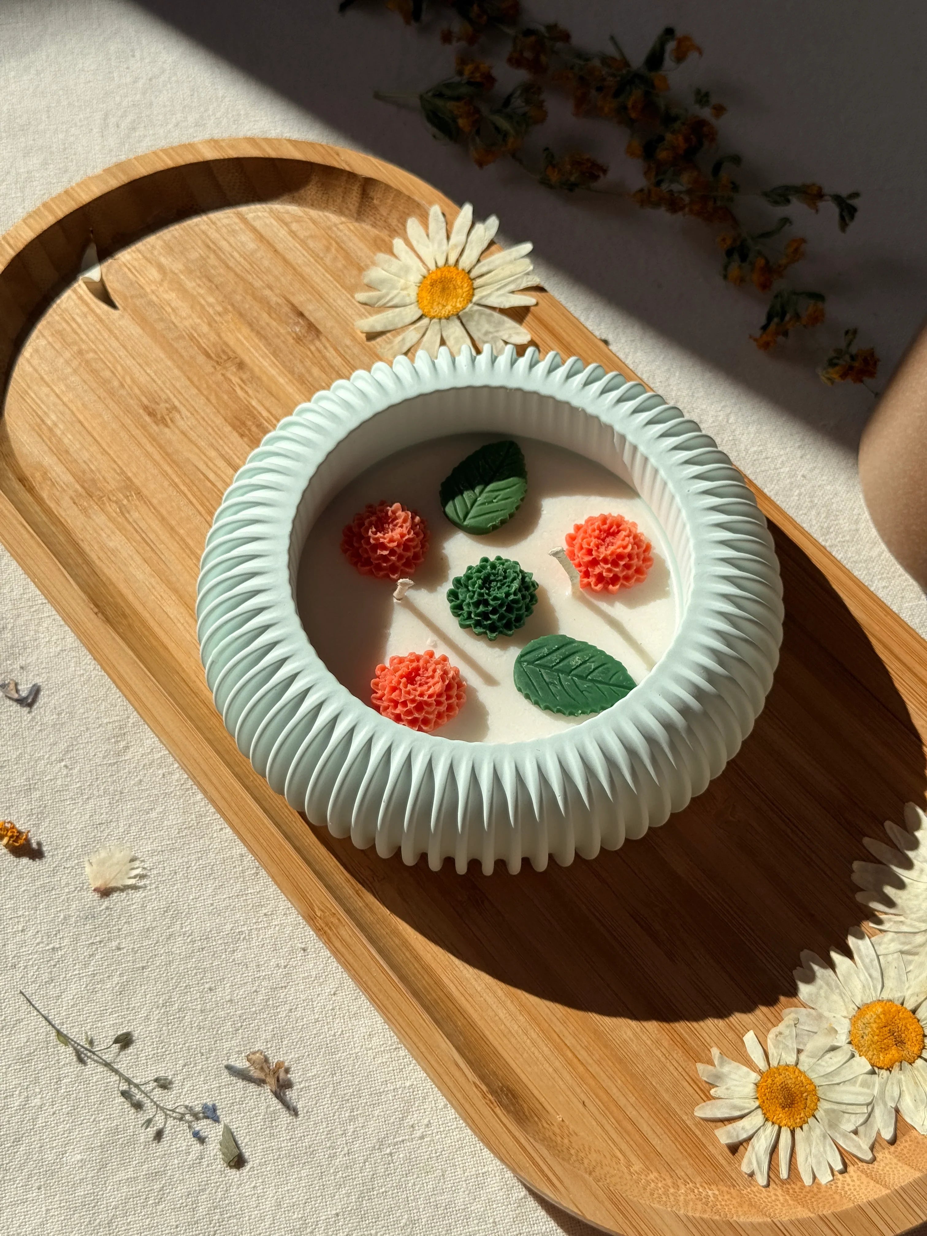 Handmade soy candle with floral wax decorations in a ribbed mint bowl, styled on wood with dried daisies