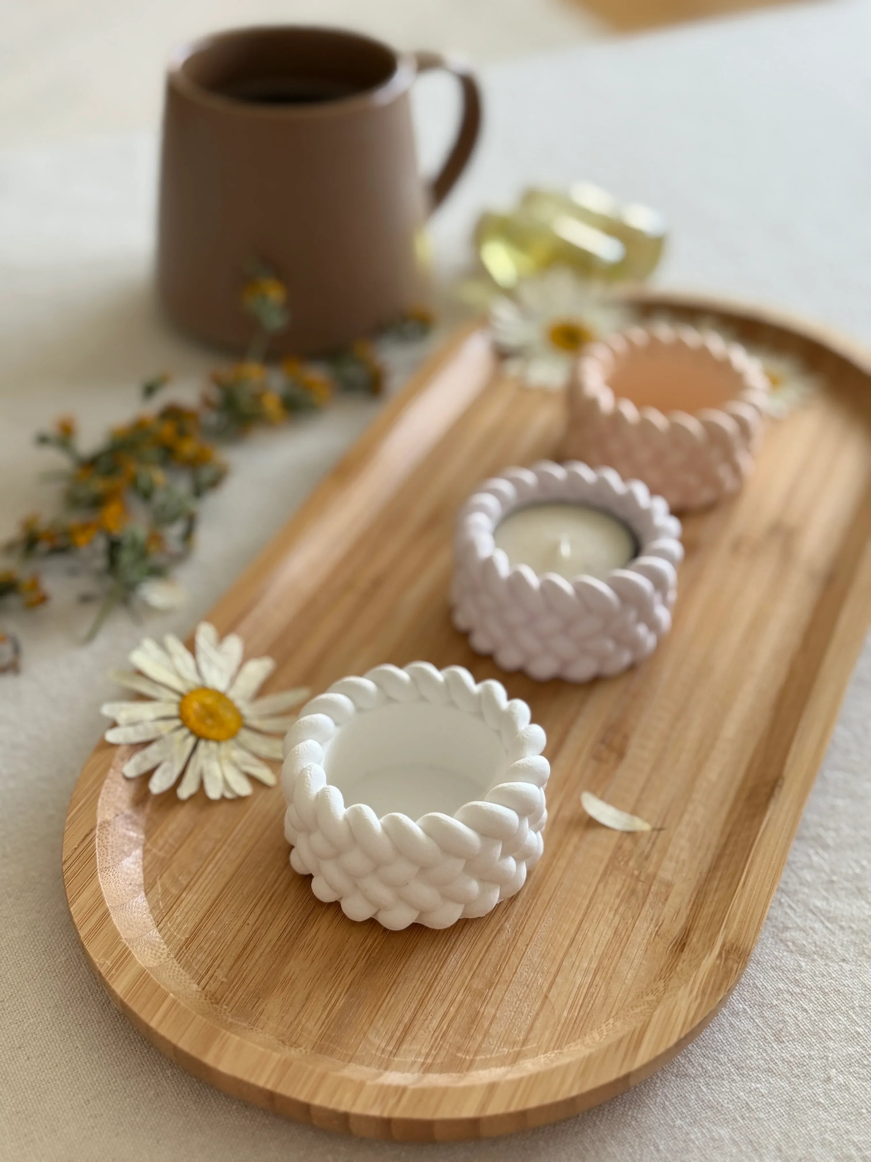 Handmade ceramic candle holders with braided texture on wooden tray, styled with daisies and mug for cozy Scandinavian home décor
