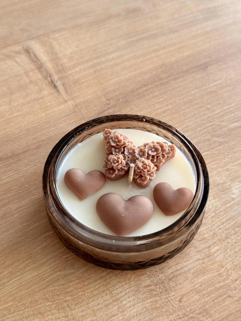 Handmade soy candle with heart and floral wax designs in a glass jar, perfect for cozy home décor.