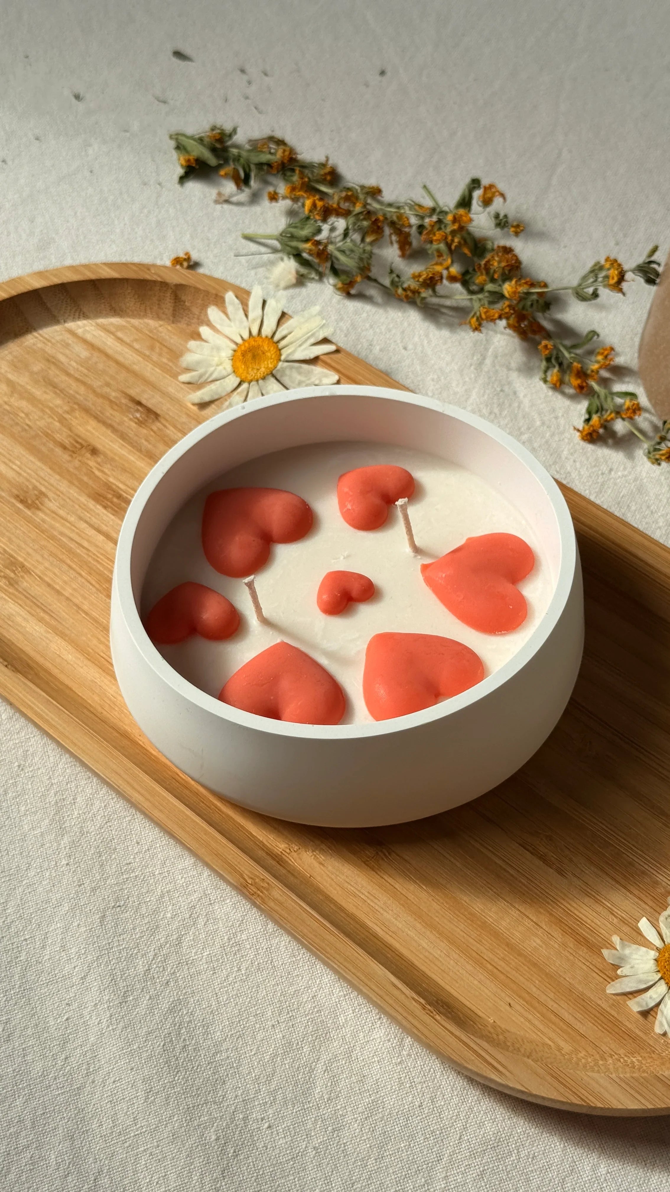Handmade soy candle with coral hearts in white ceramic bowl, styled with dried flowers on wooden tray