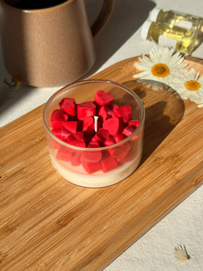 Red heart-shaped soy candle in glass jar on wooden tray with daisies, cozy home decor