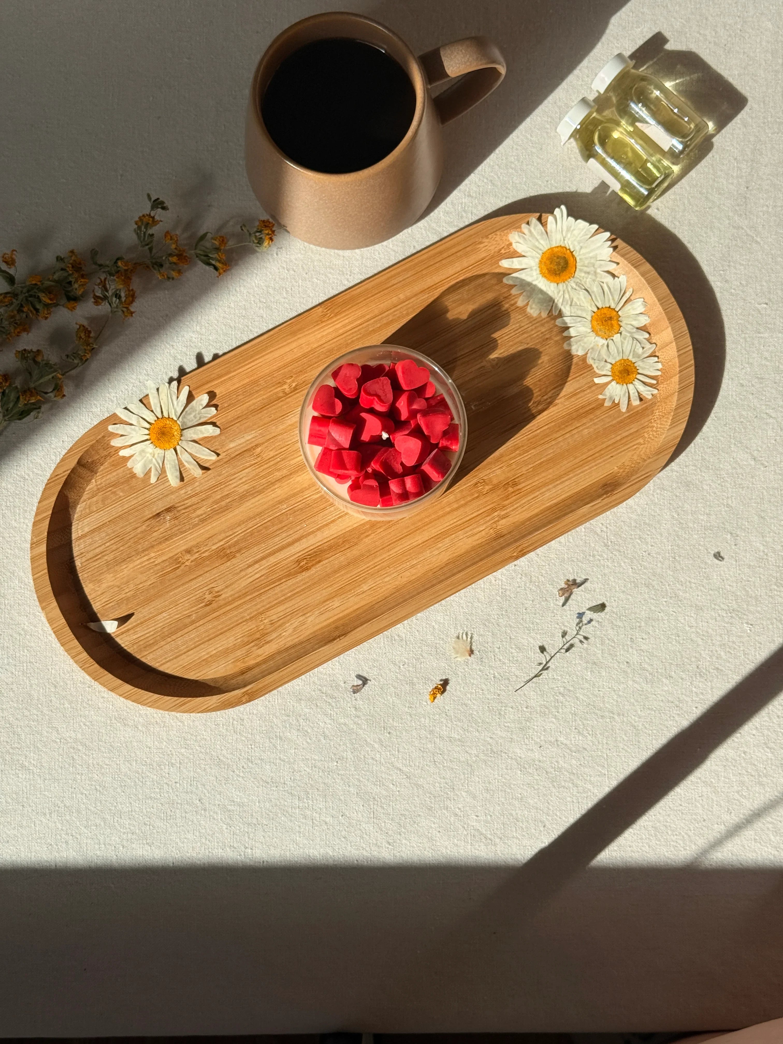 Red heart-shaped soy wax melts in glass jar on wooden tray with daisies, coffee mug, and dried flowers for cozy home ambiance