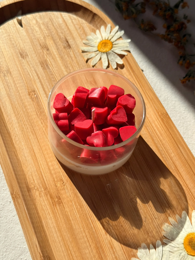 Red heart-shaped soy wax melts in glass jar on wooden tray with daisies, cozy home decor