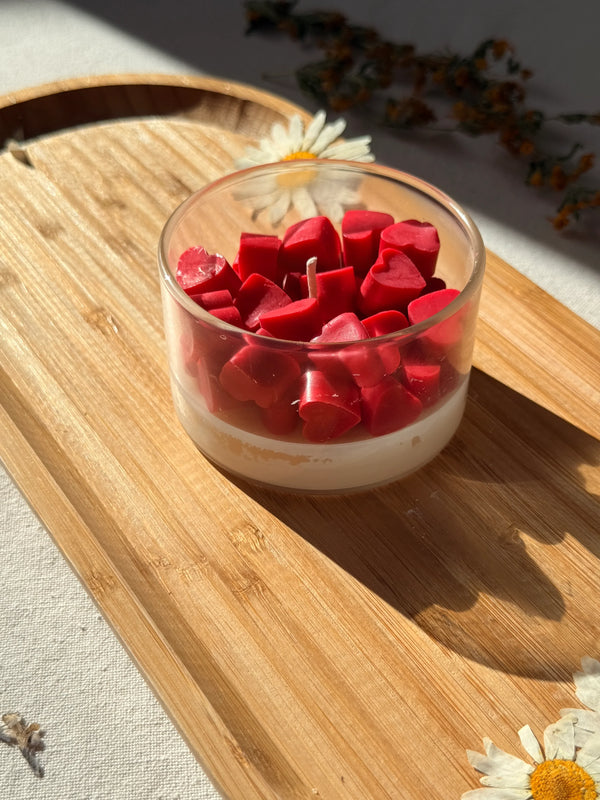 Red heart-shaped soy wax melts in glass jar on wooden tray with daisies, Scandinavian home decor