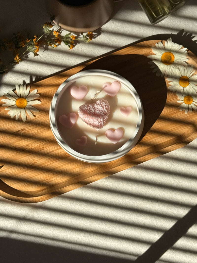 Handmade soy candle with pink heart decorations, daisies, and warm sunlight on wood tray