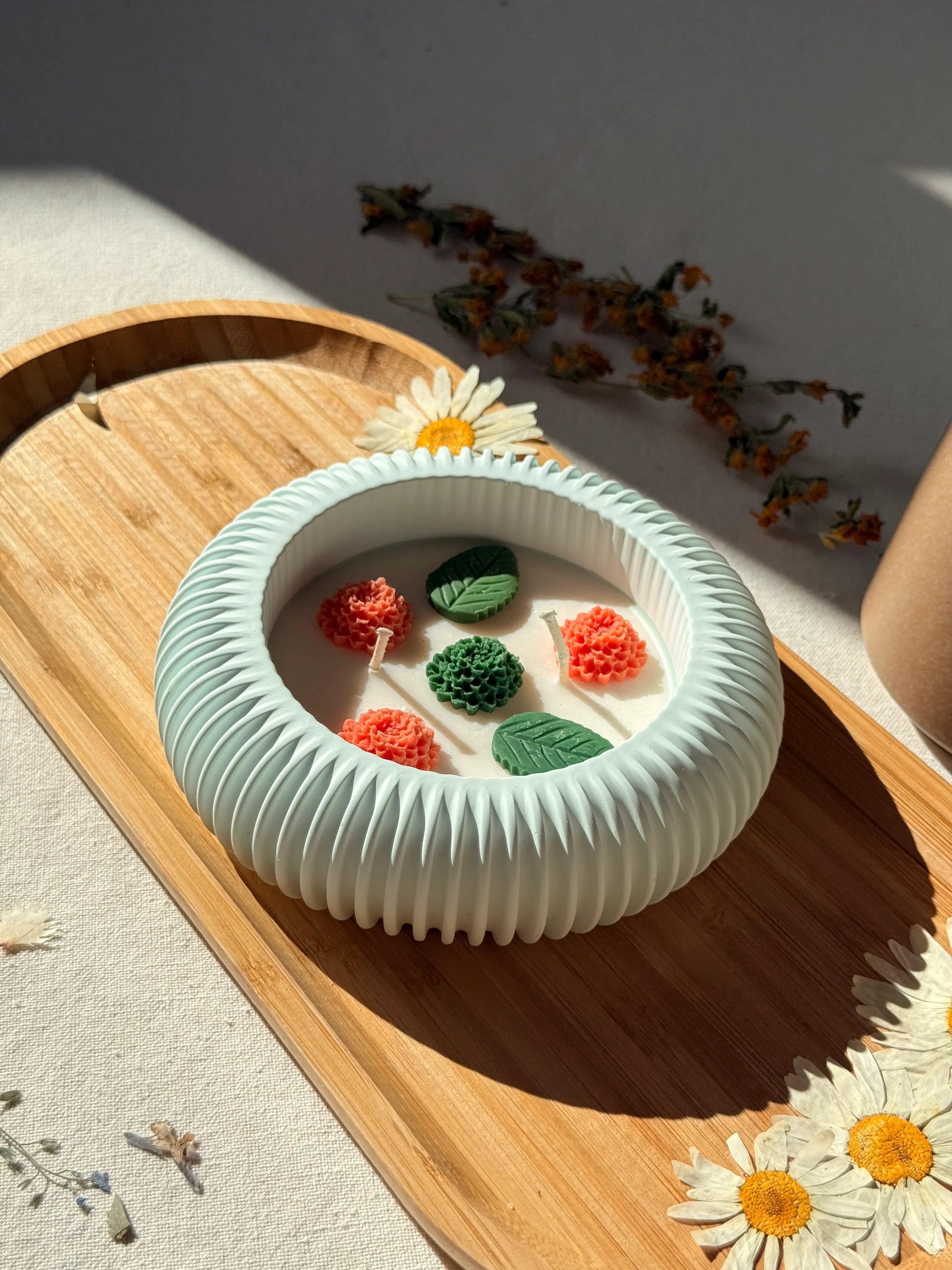 Handmade soy candle with floral wax accents in a ribbed ceramic bowl, styled with dried daisies on wood tray