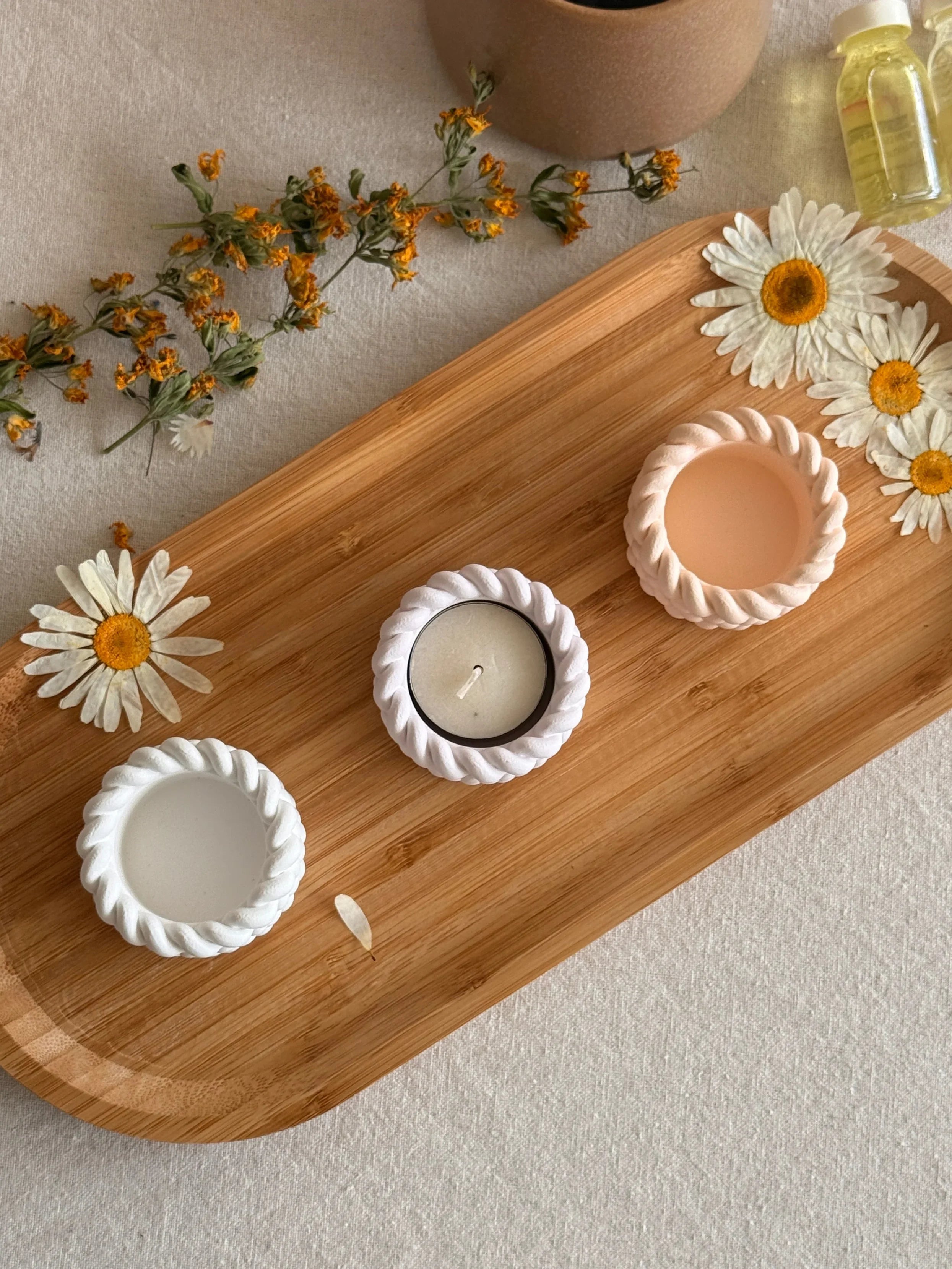 Handmade soy candles in rope-textured holders on wooden tray with dried daisies, Scandinavian home decor