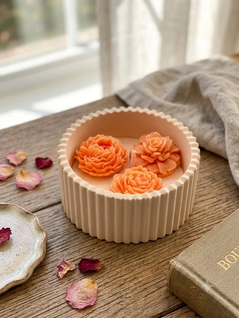 Handmade soy candle with rose-shaped wax blooms in a ribbed ceramic holder, styled with dried petals and a vintage book.