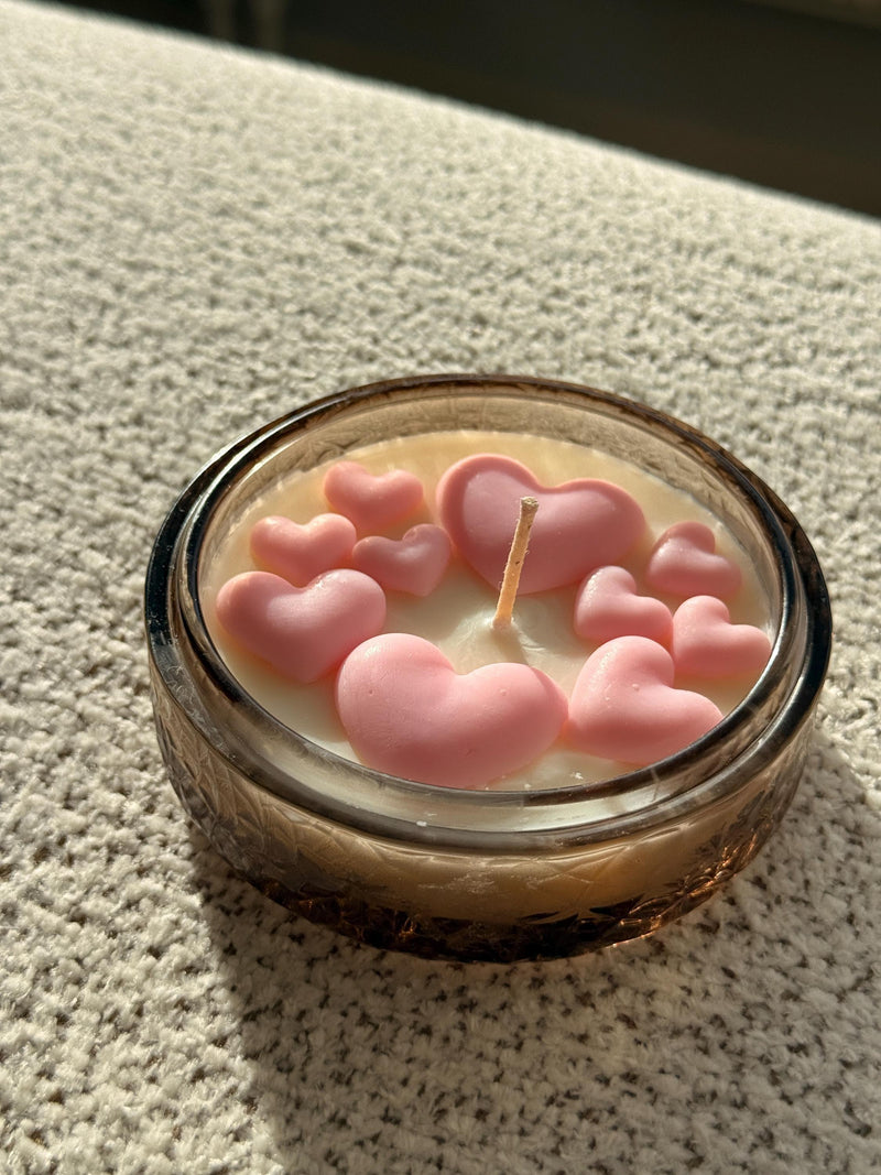Handmade soy candle with pink heart decorations in a glass jar, perfect for cozy home décor or thoughtful gifts.